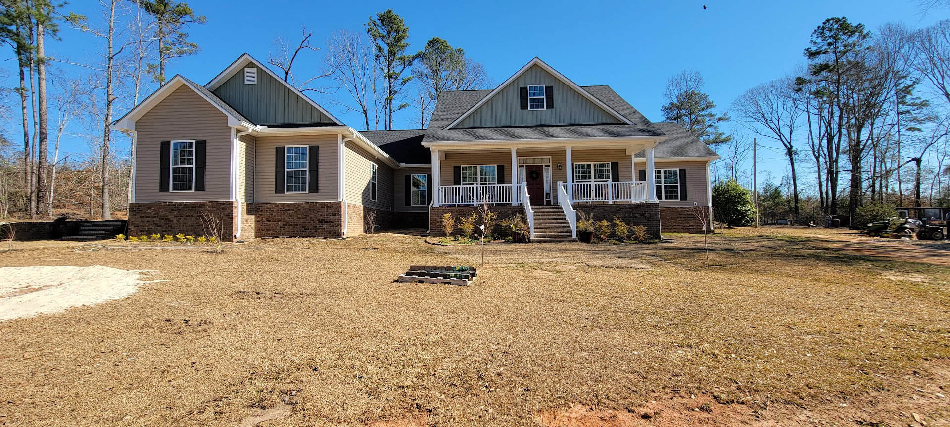 Two-story house with white roof, multi-pane windows, wooden porch, white railing, and green lawn bordered by a wooden fence
