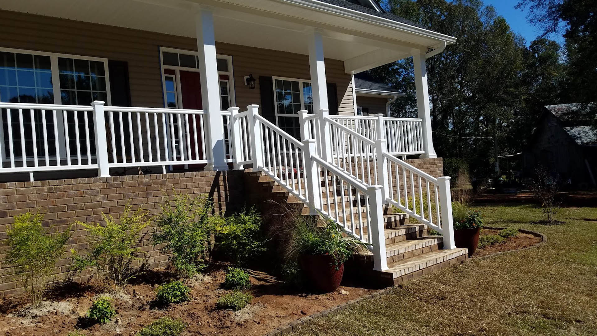 Front porch with white railing and stairs, potted plant beside steps, light-colored siding, landscaped garden area