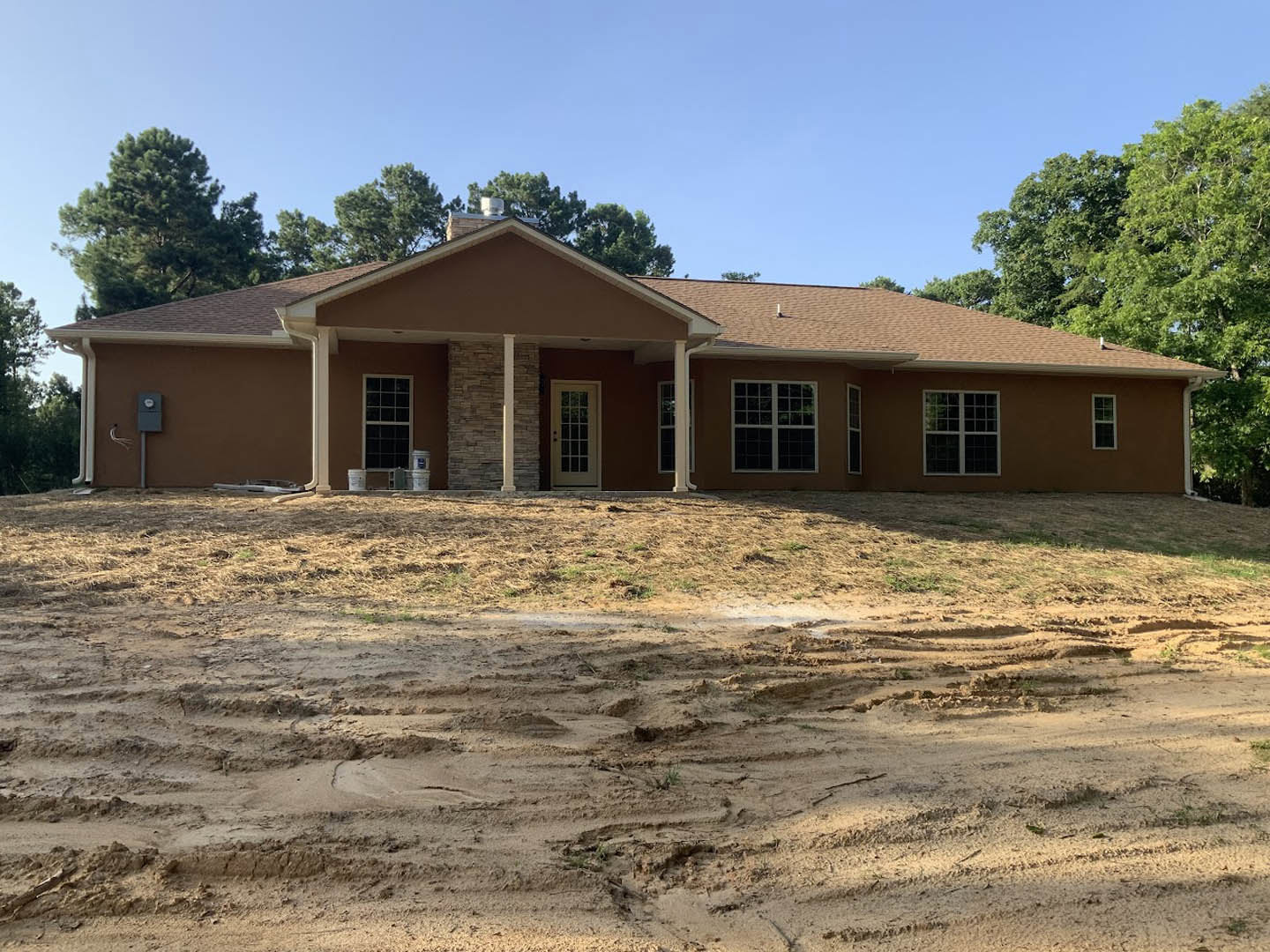Two-story house with stone and white siding, glass-paneled front door, multi-pane windows, and unfinished dirt yard in foreground