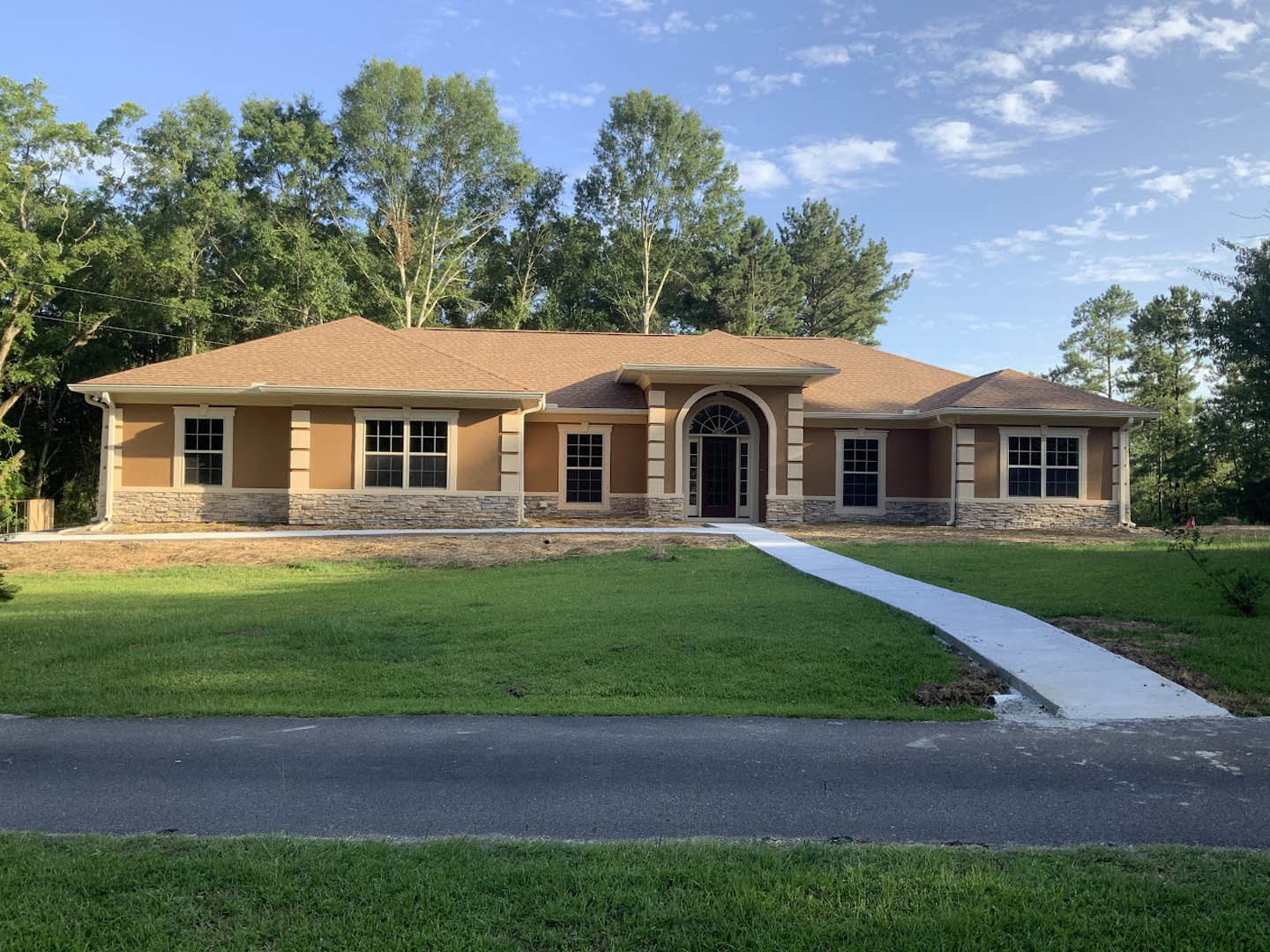 Two-story house with white-framed door and multiple square-paned windows, concrete path beside green lawn, mature trees and historic Hyde Hall visible in the background.