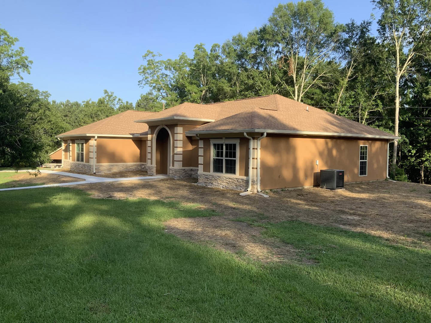 Two-story home with white-trimmed windows, dark front door, manicured lawn, mature trees in background, and black vent near entryway