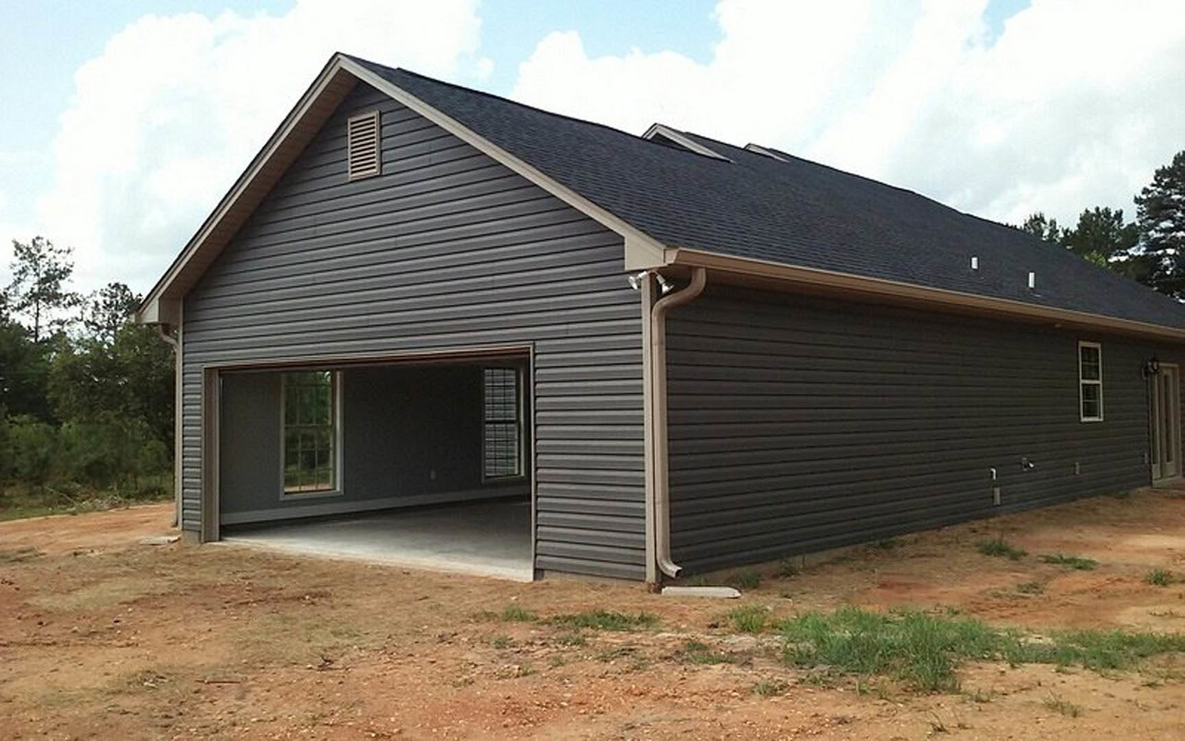 Detached garage with paneled door, white siding, roof gutter, and vent, set in front of historic Jarrell Plantation with trees and cloudy sky in background
