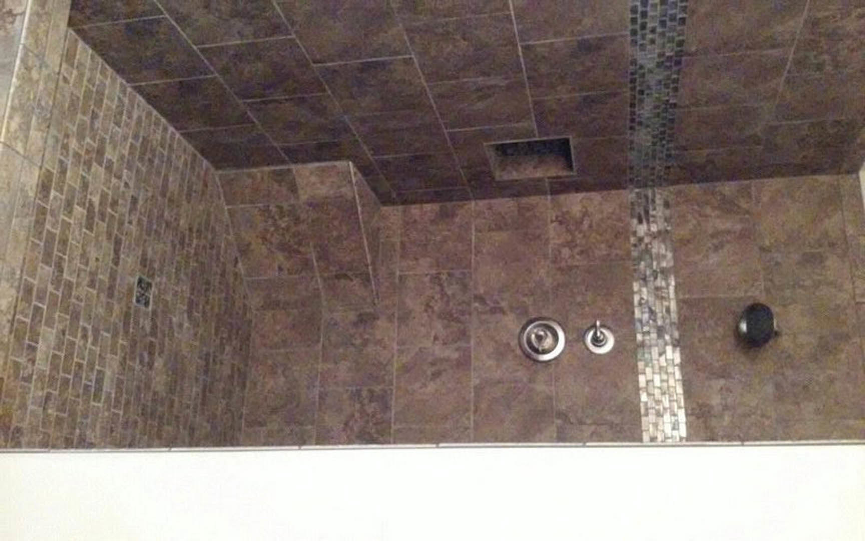 Walk-in shower with light gray tile walls and ceiling, recessed vent, and glass enclosure