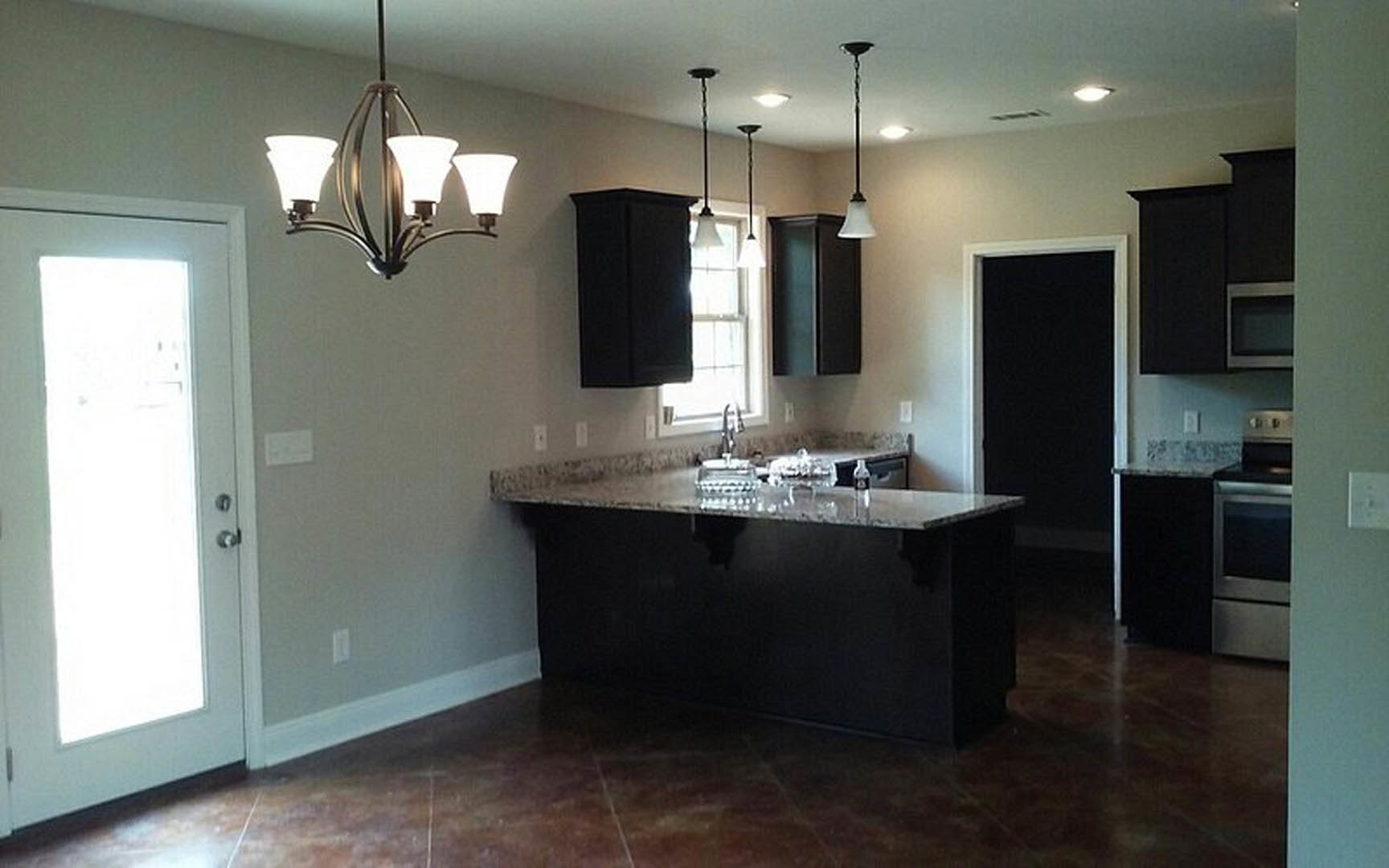 Spacious kitchen featuring tile flooring, white cabinetry, stone countertops, stainless steel sink, and a decorative chandelier hanging from the ceiling.