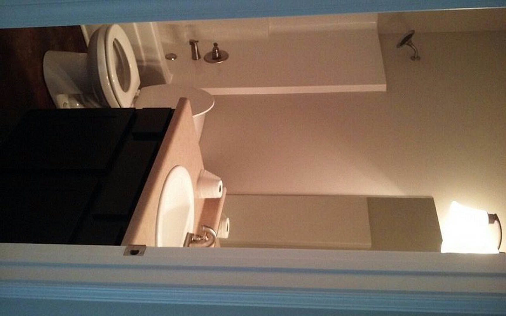 Modern bathroom featuring a white porcelain sink with chrome faucet, wall-mounted mirror above, and a toilet with lid open, set against light-colored tile walls.