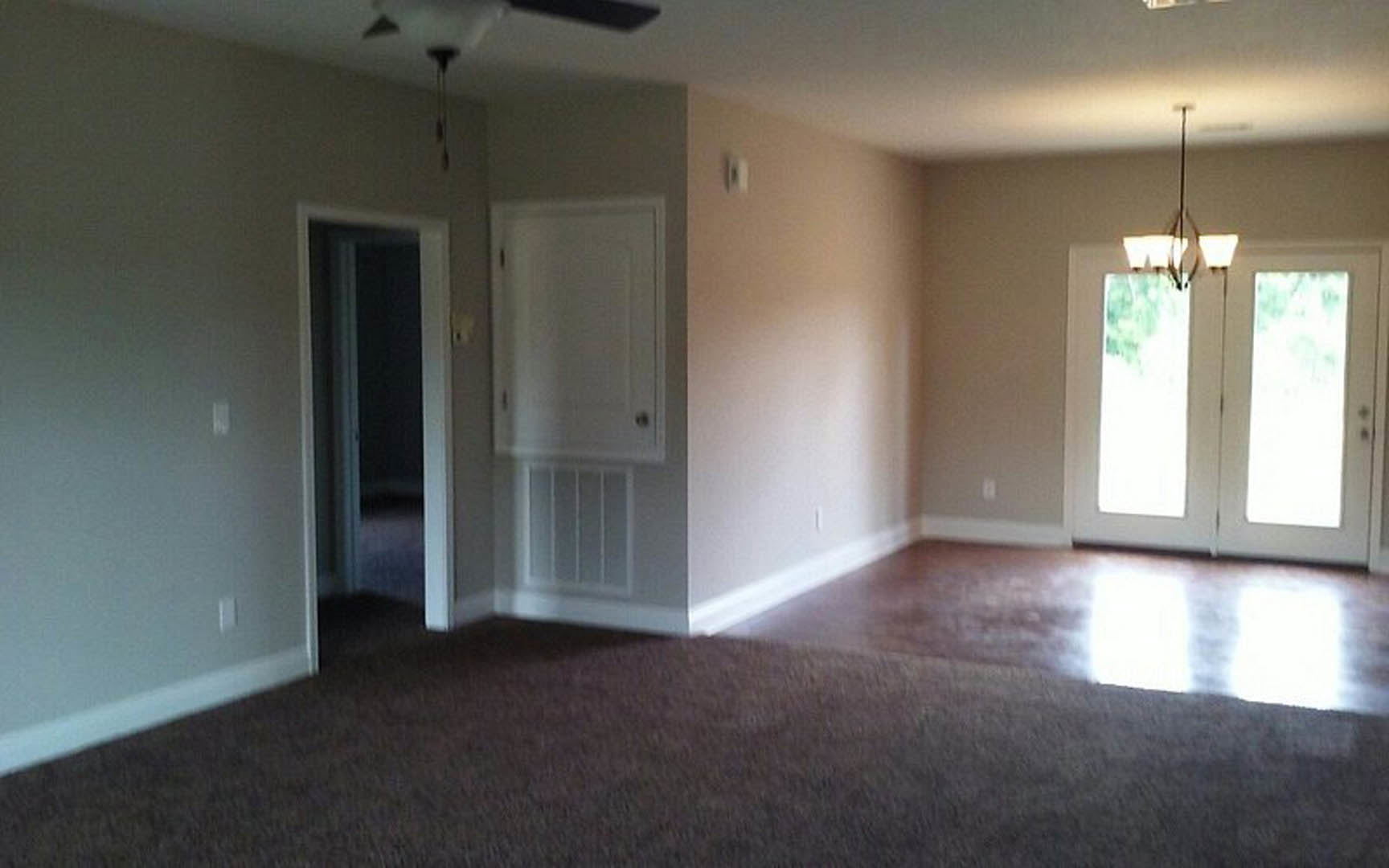 Living room with double white doors, carpeted floor, light fixture on ceiling, plaster walls, and vented door