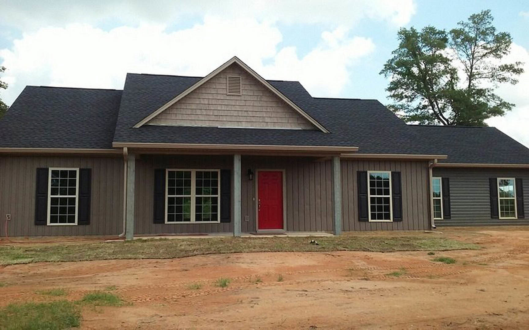 White cottage-style home exterior with red front door, white-trimmed windows, leafy green tree, and cloudy sky in background