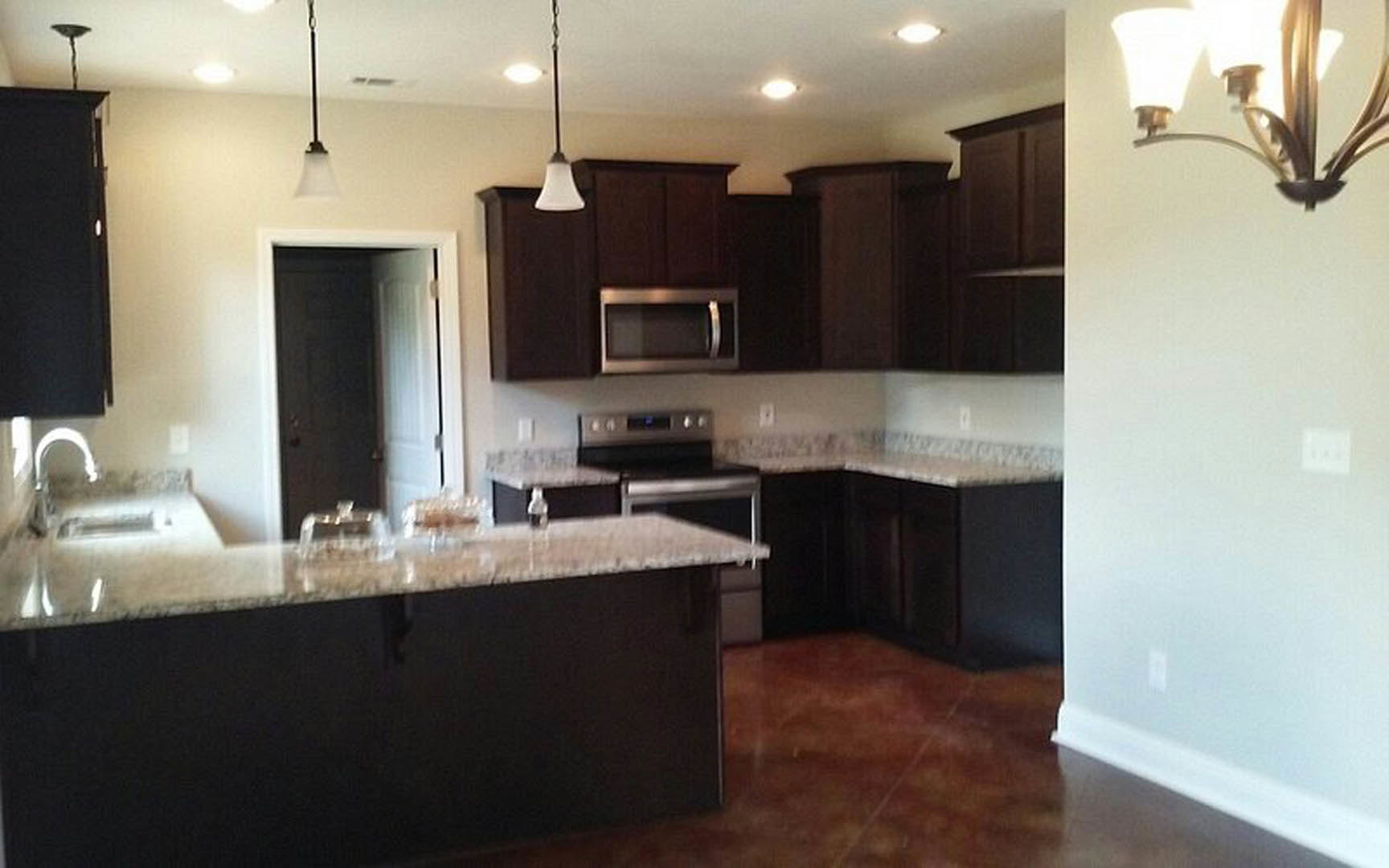 Kitchen with dark wood cabinets, light stone countertops, stainless steel sink, and white walls with a light switch.