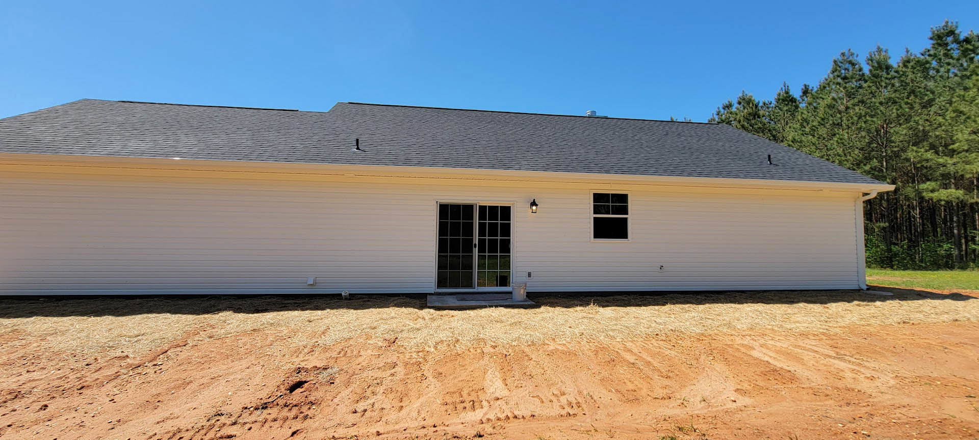 White house with multi-pane windows, white siding, sliding glass door, and dirt yard in foreground