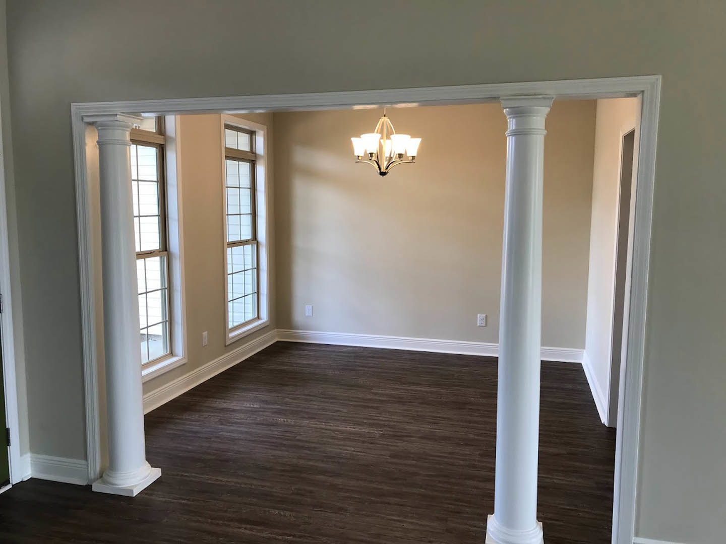 Wood floor room with white pillars, five-light chandelier, white-framed window, and plaster walls with molding