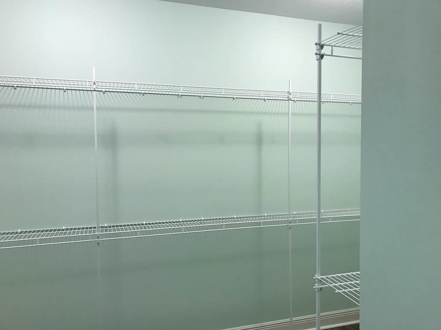 White metal shelving unit mounted on a blue-accented wall in a bathroom, with a mirror and shower visible in the background.