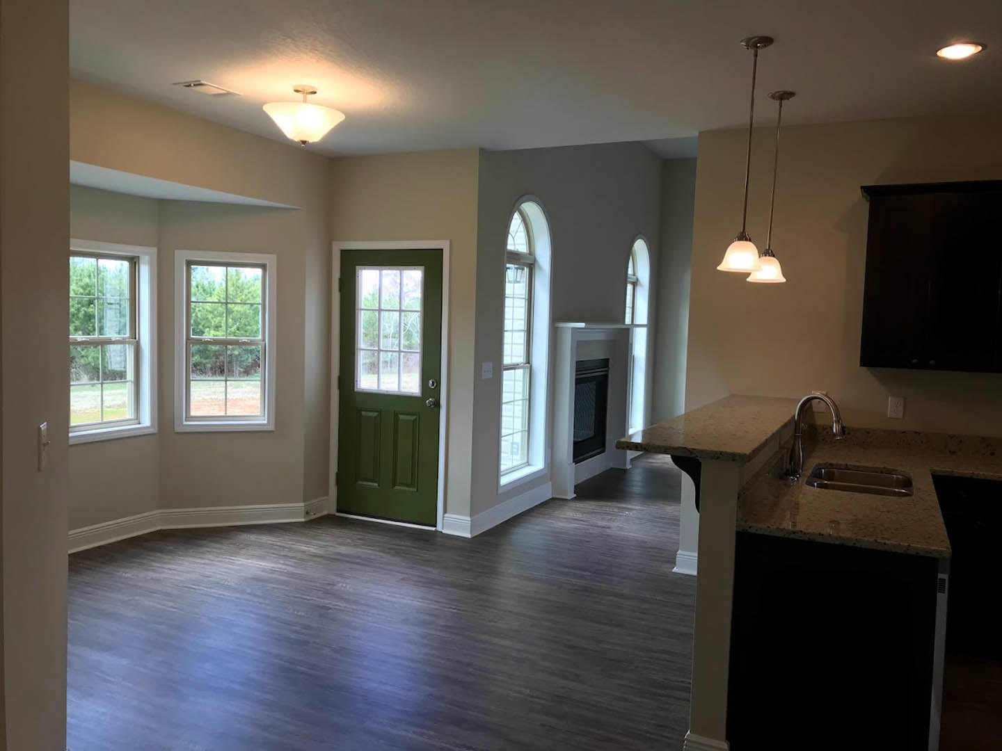 Open kitchen and living room featuring light laminate flooring, black accent wall with sconce, green door with window, large window overlooking trees, and black oven integrated