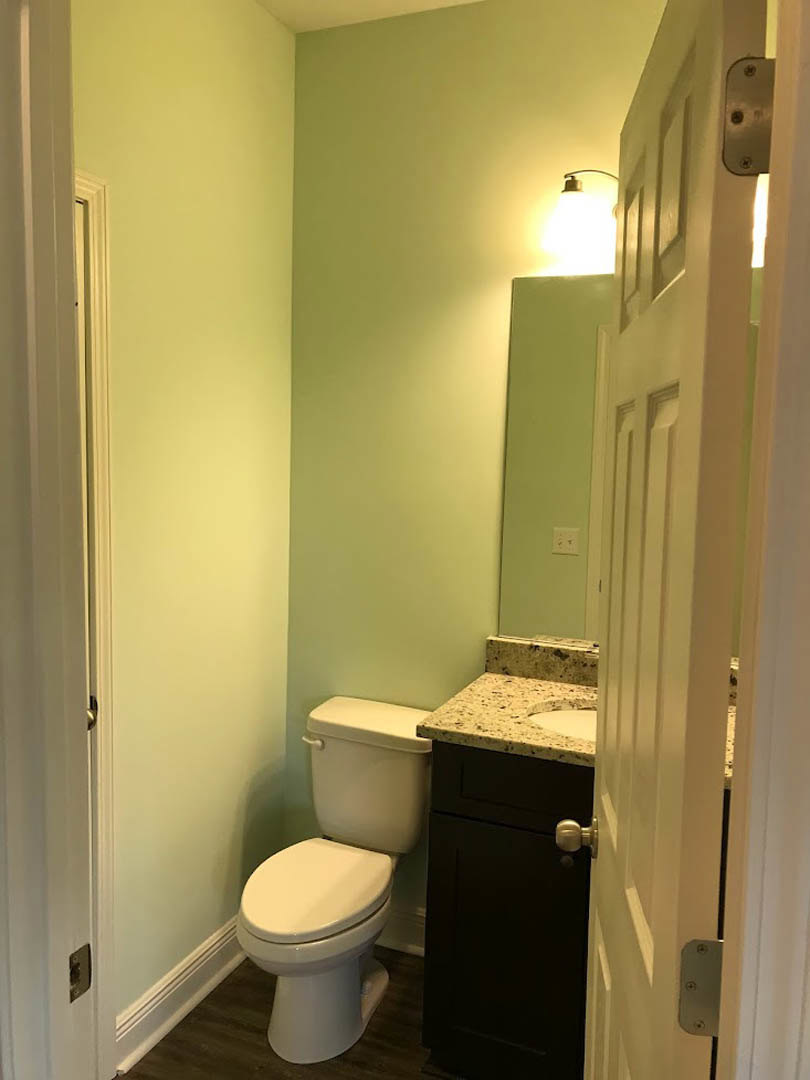 White porcelain toilet and sink with chrome faucet, light-colored tile walls, wood door with keyhole, illuminated bulb overhead, small mirror above countertop