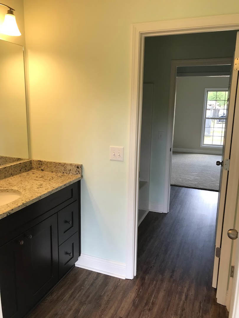 Bathroom featuring a marble countertop with undermount sink, wood plank flooring, white cabinetry, wall-mounted light switch, and window overlooking parking lot