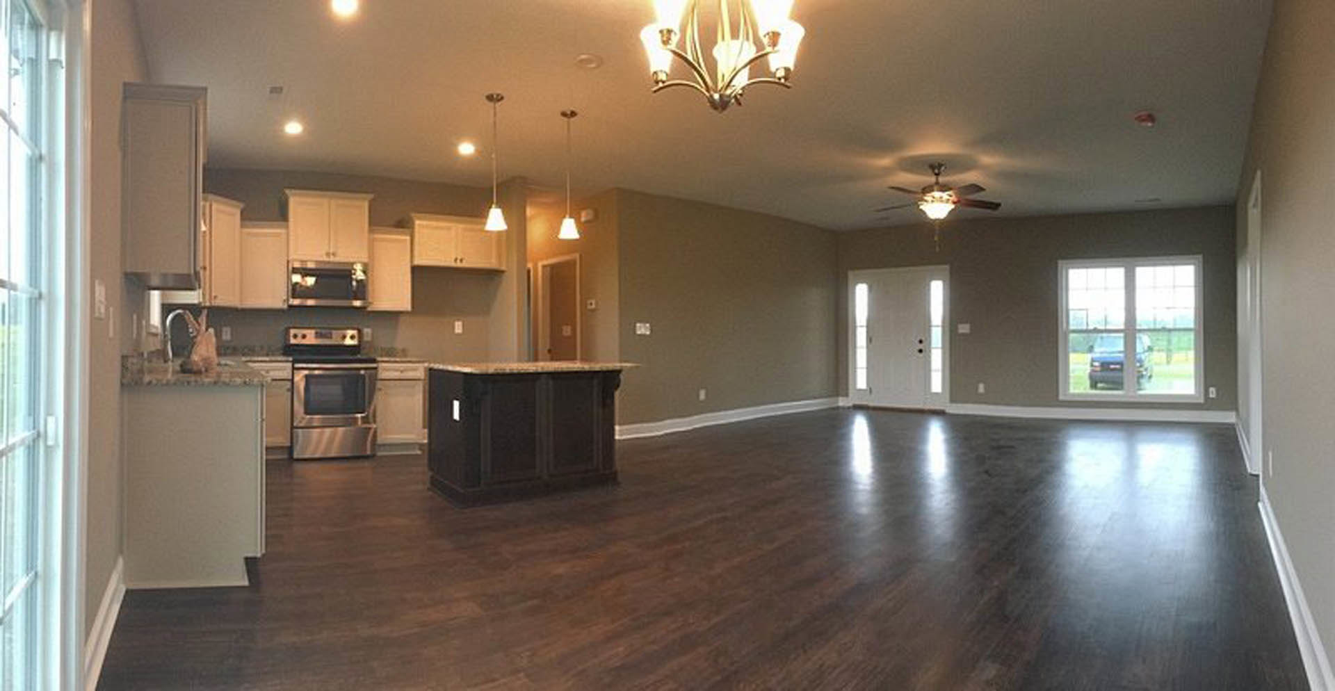 Open-concept kitchen and living room featuring hardwood floors, black marble countertop, white cabinetry, stainless steel microwave, modern light fixture, and large window with a