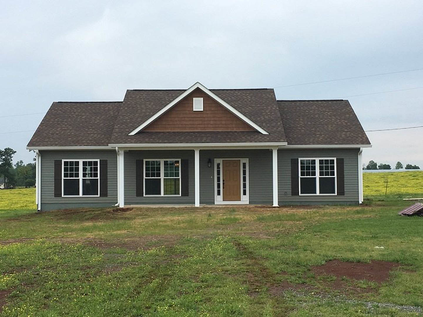 Two-story home with white siding, brown front door with white trim, large window with white frame, covered porch supported by white column, green lawn in front, partly cloudy sky