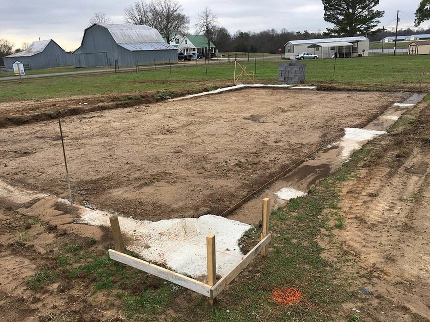Dirt foundation bordered by wooden framing in grassy field with trees and open sky