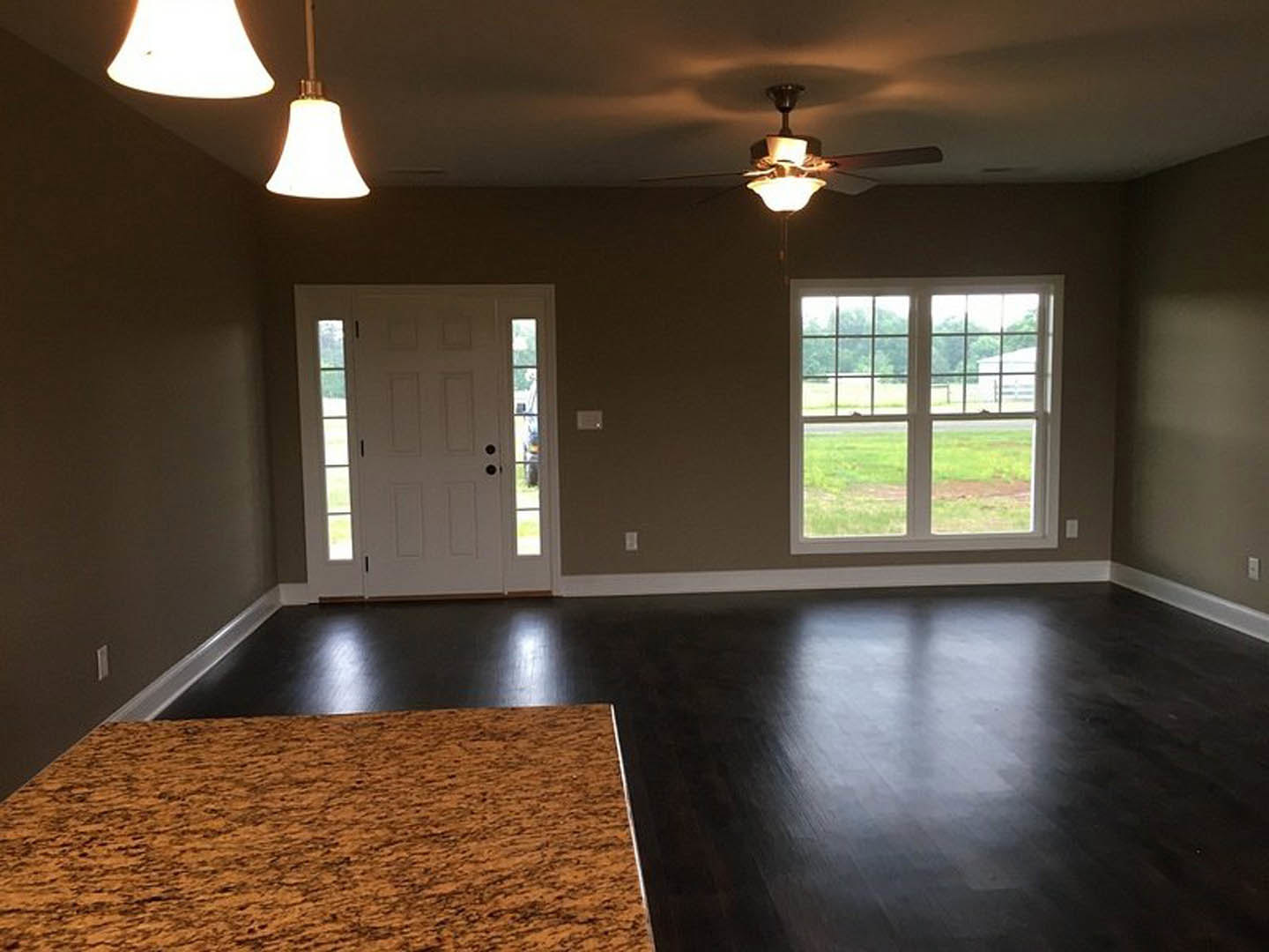 Living room with laminate flooring, ceiling fan, white door with glass panels, window overlooking grassy yard and barn, brown and black floor, close-up of light fixture