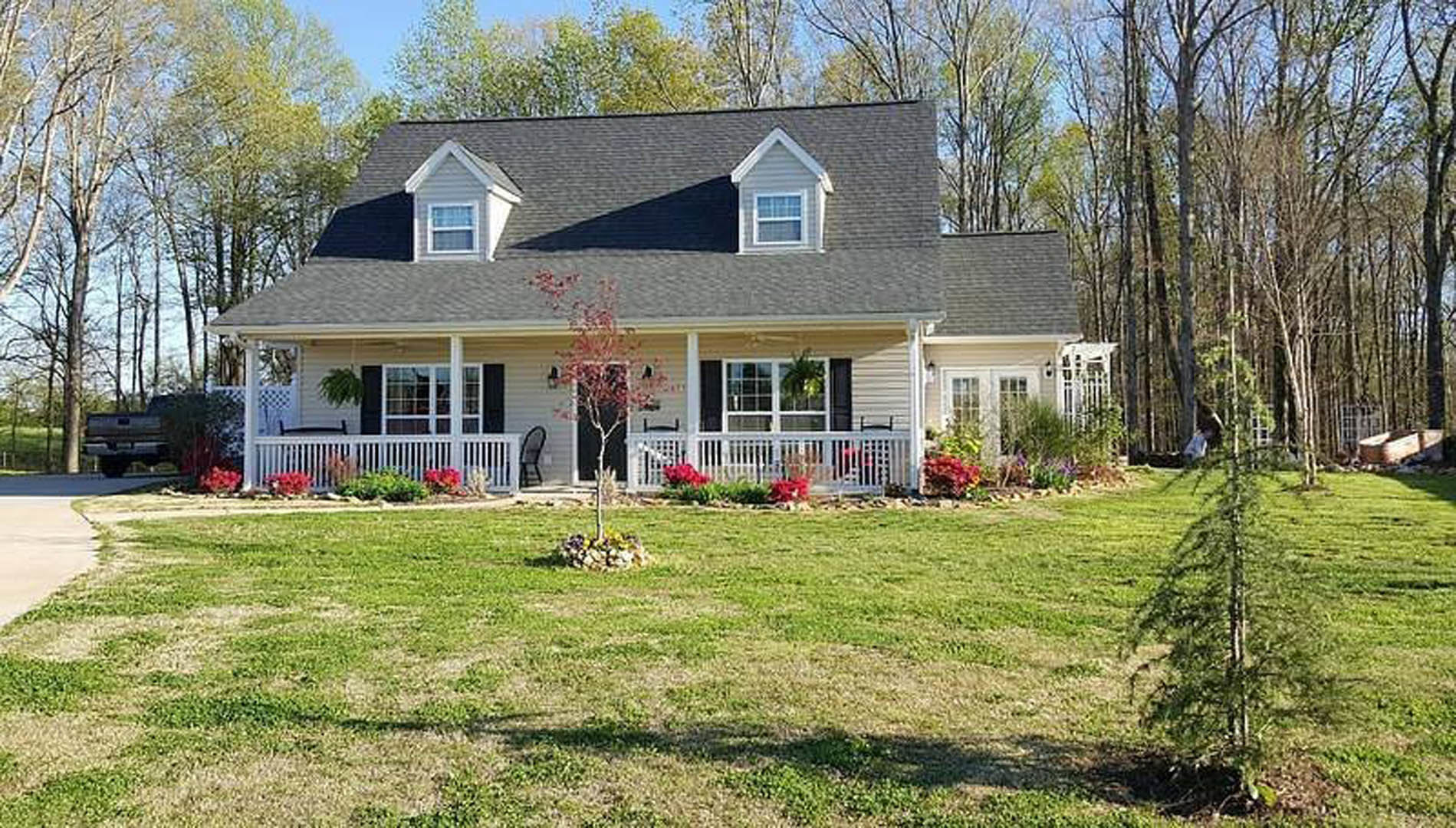 Two-story house with white multi-pane windows, covered front porch, green lawn, and mature trees in the yard