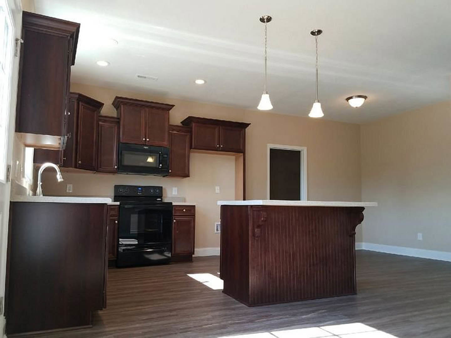 Brown wood kitchen bar with white countertop, black stove and oven, dark wood cabinets, white walls, and built-in microwave.