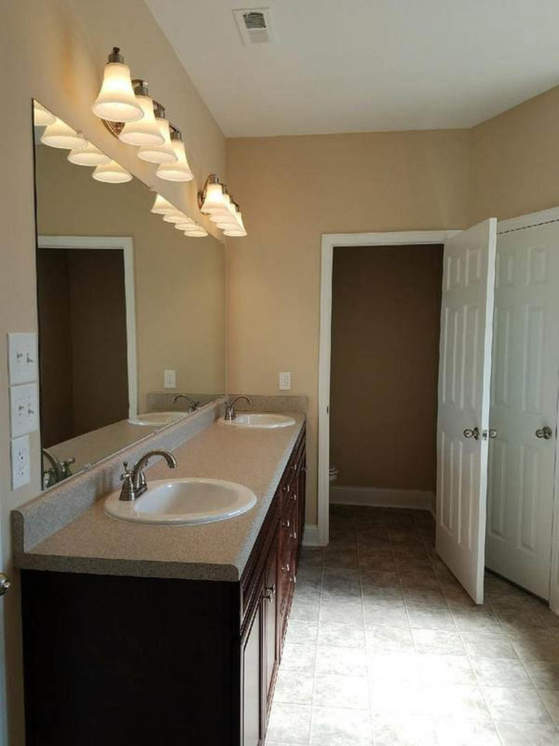 Bathroom with double vanity featuring two undermount sinks, wide framed mirror above, white cabinetry, chrome faucets, tile flooring, and recessed lighting.