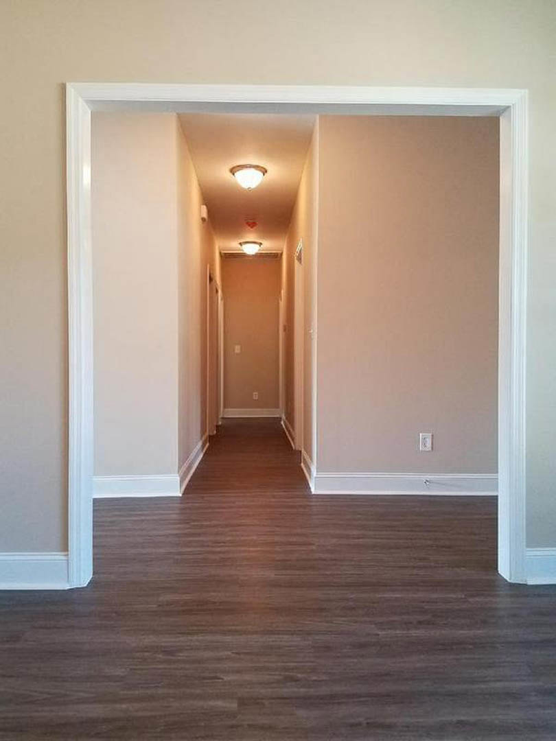 Hallway with wood flooring, white plaster walls, ceiling-mounted light fixture, open door, and visible light switch
