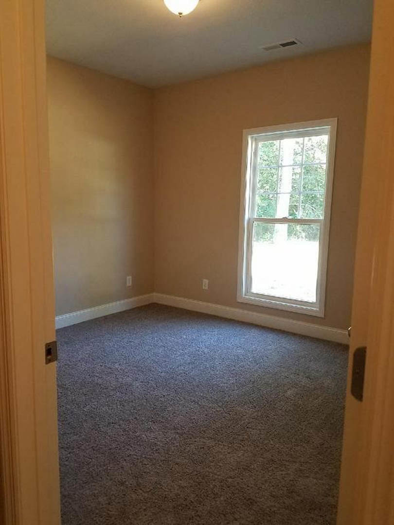 Carpeted bedroom with white-framed window, paneled door, plaster walls, and ceiling light fixture