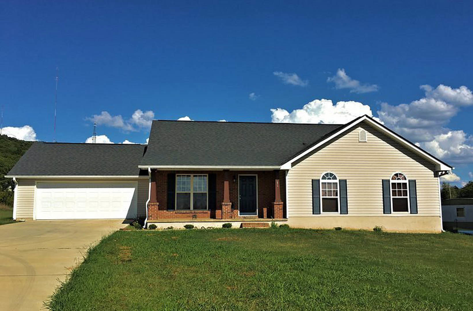 Red brick house with black front door framed in white, large windows, manicured green lawn, and covered porch under partly cloudy sky