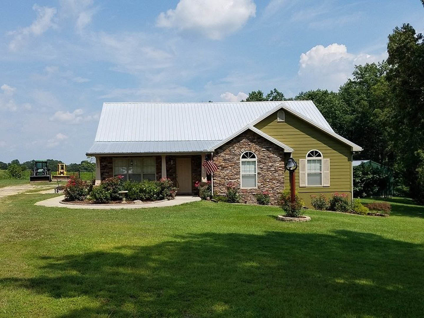 Two-story farmhouse with stone accent wall, white-framed windows, American flag by front entrance, green lawn, blue sky, and trees in background