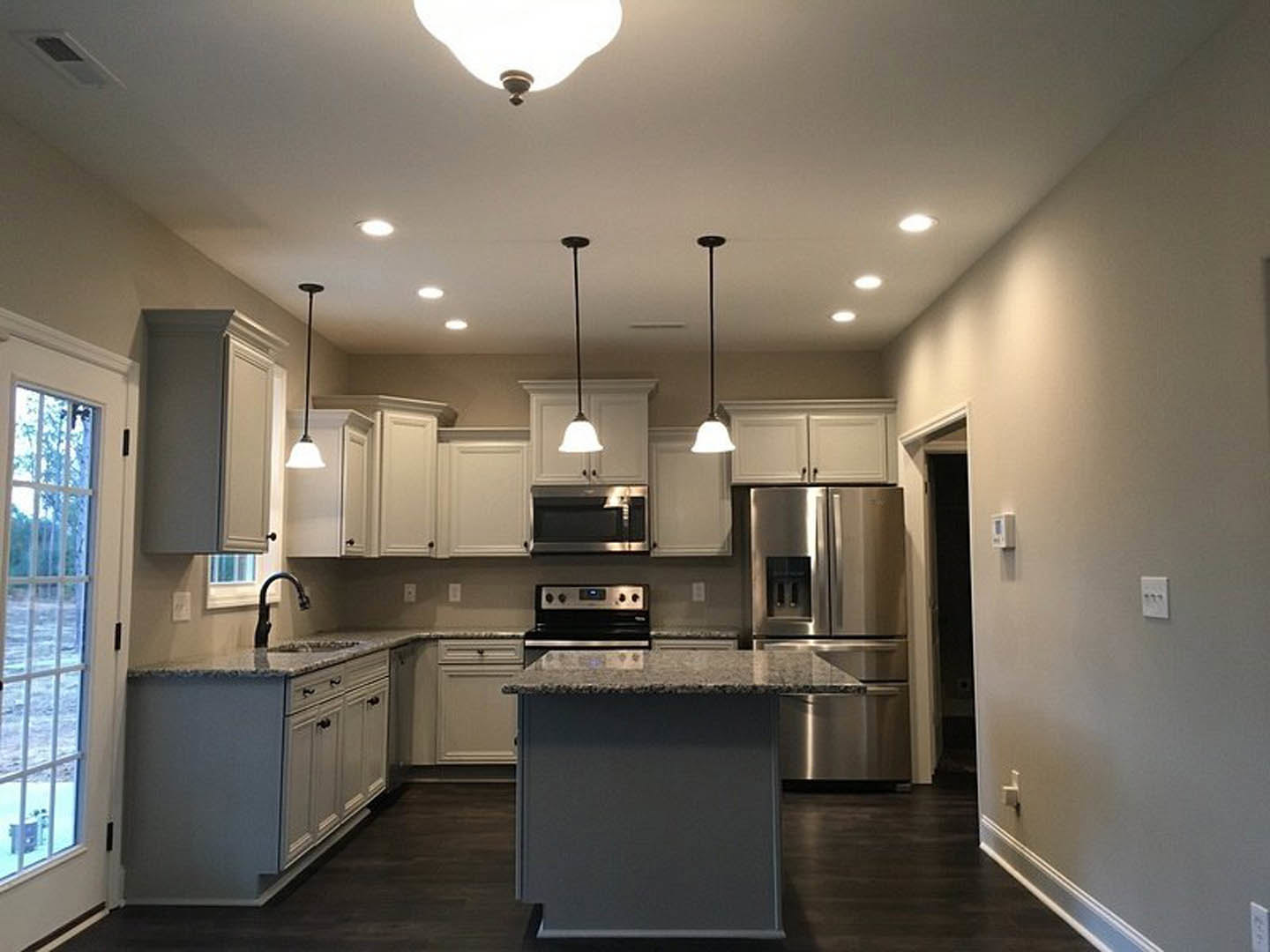 Spacious kitchen featuring a large granite-topped island, stainless steel refrigerator, marble countertops, white cabinetry, and modern lighting fixtures