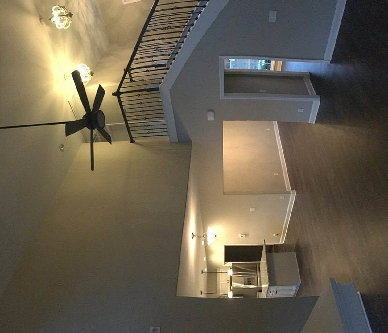 Open living area with black ceiling fan, white walls, staircase with wooden steps and white railing, white door with matching trim, hardwood flooring