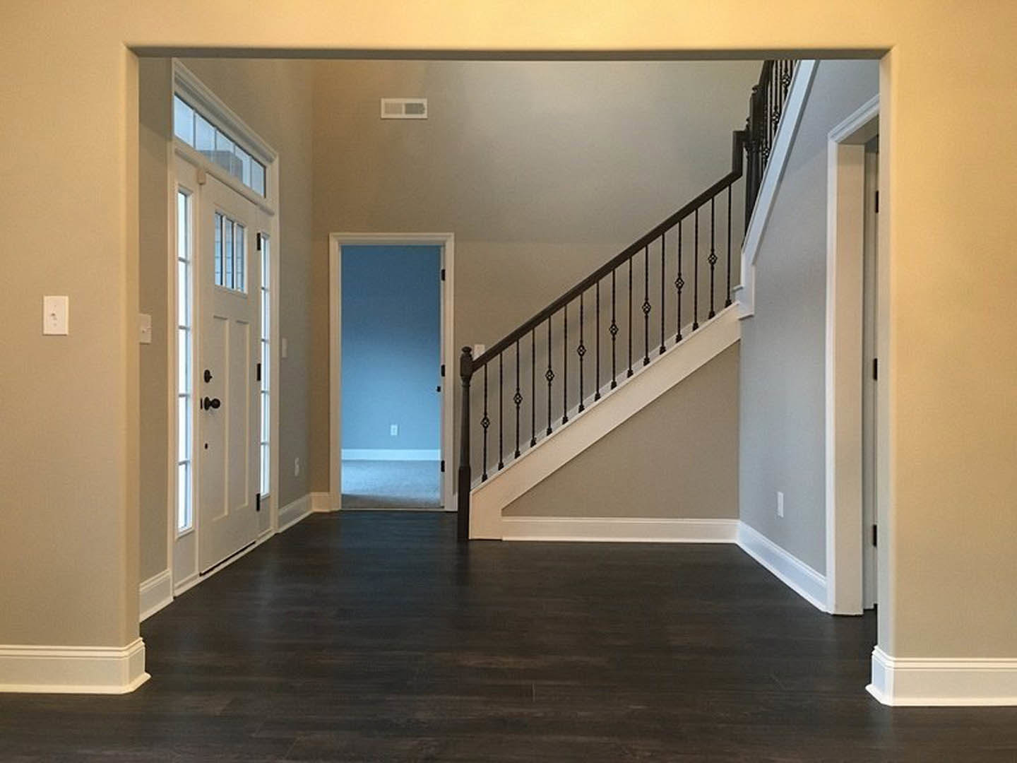 Hallway with dark wood flooring, white walls, a staircase featuring a metal handrail, and multiple white doors with window panels