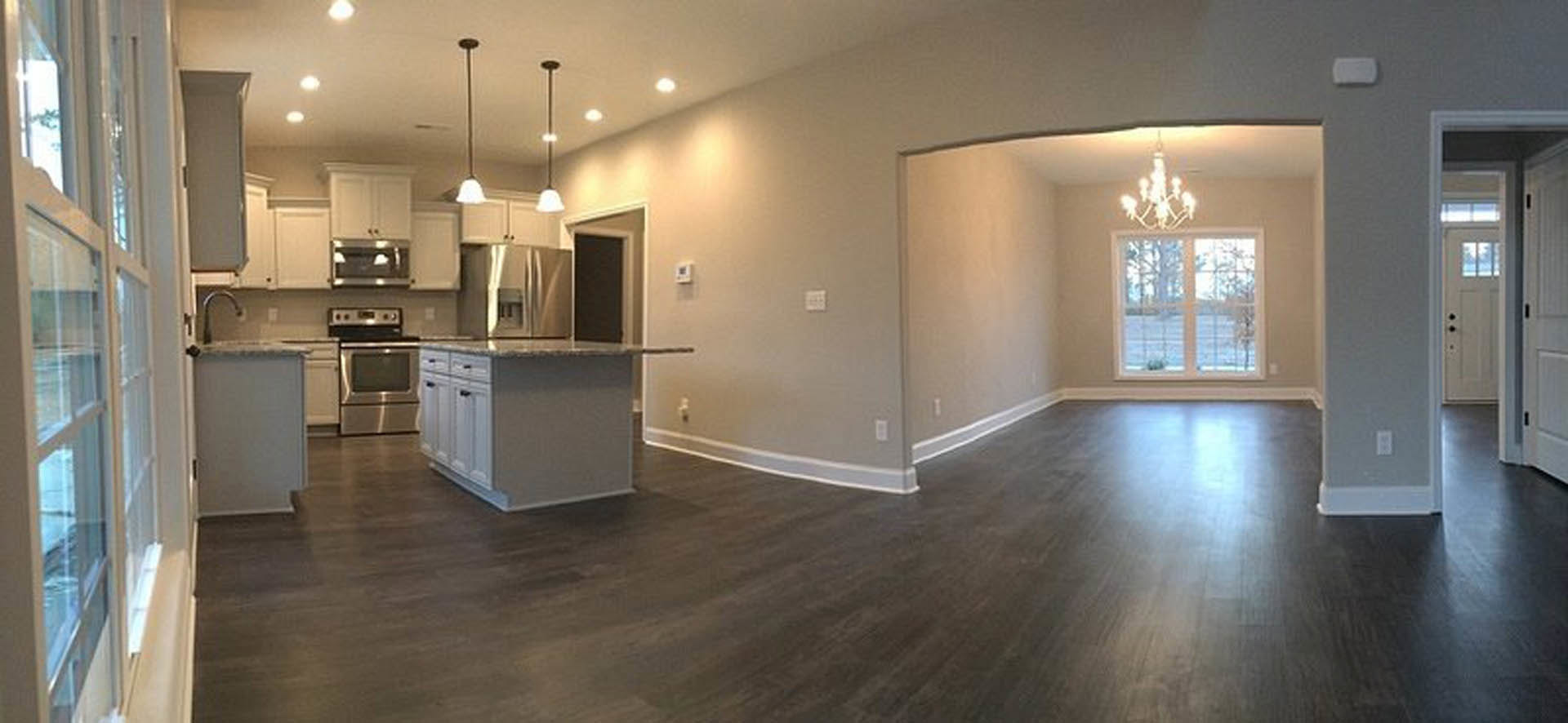 Open kitchen and dining area featuring dark hardwood floors, white cabinetry, gray countertops, stainless steel appliances, large window with outdoor view, and white trim along the