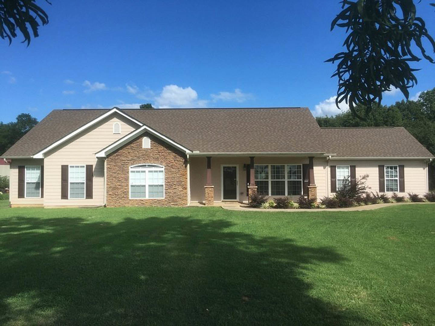 Brick exterior home with white-framed windows, green lawn in front, tree casting shadow across grass, leafy trees in background