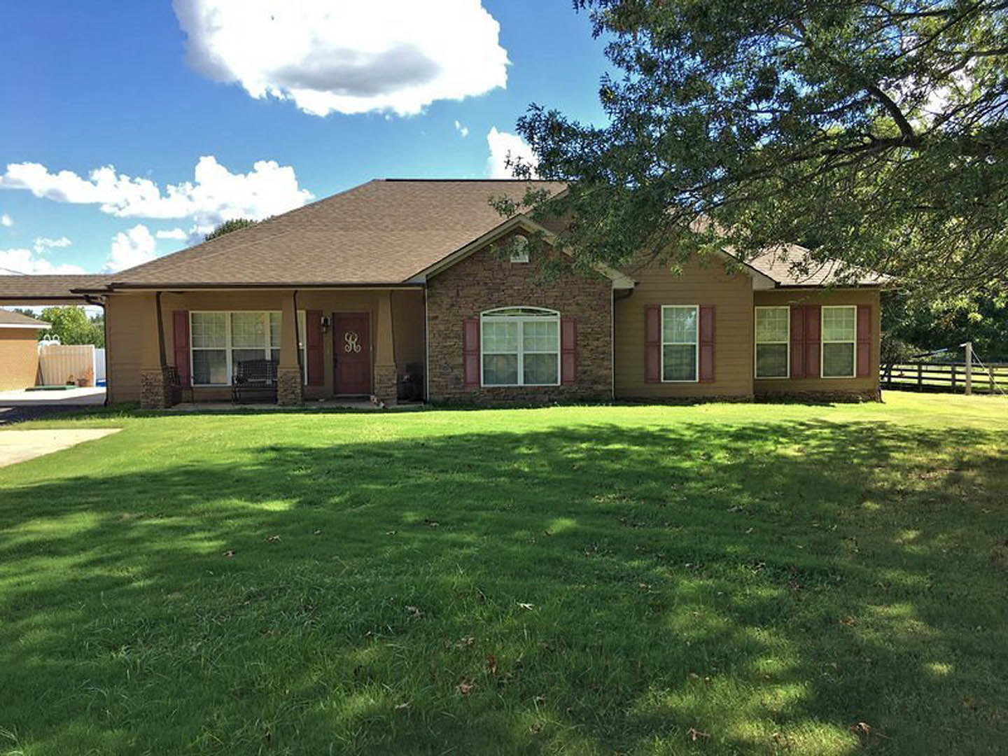 Modern two-story home with white siding, large windows, covered porch, manicured green lawn, mature tree, and cloudy sky overhead