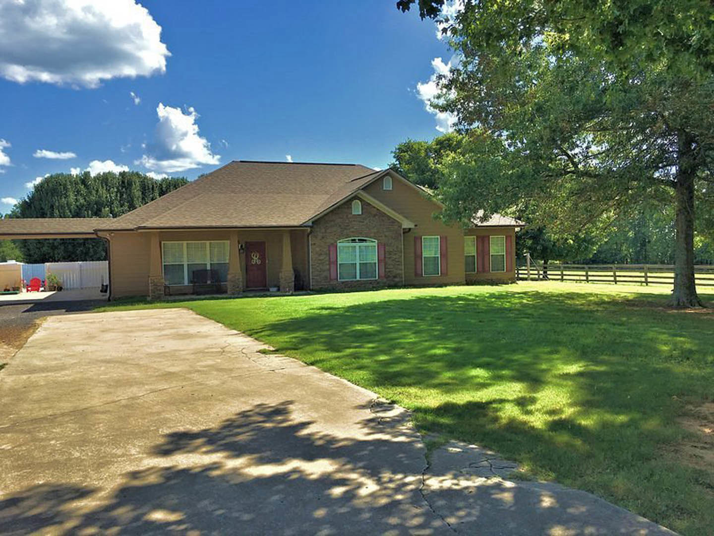 Two-story home with white siding, red front door, fenced yard, concrete driveway, large windows, green lawn, and mature trees