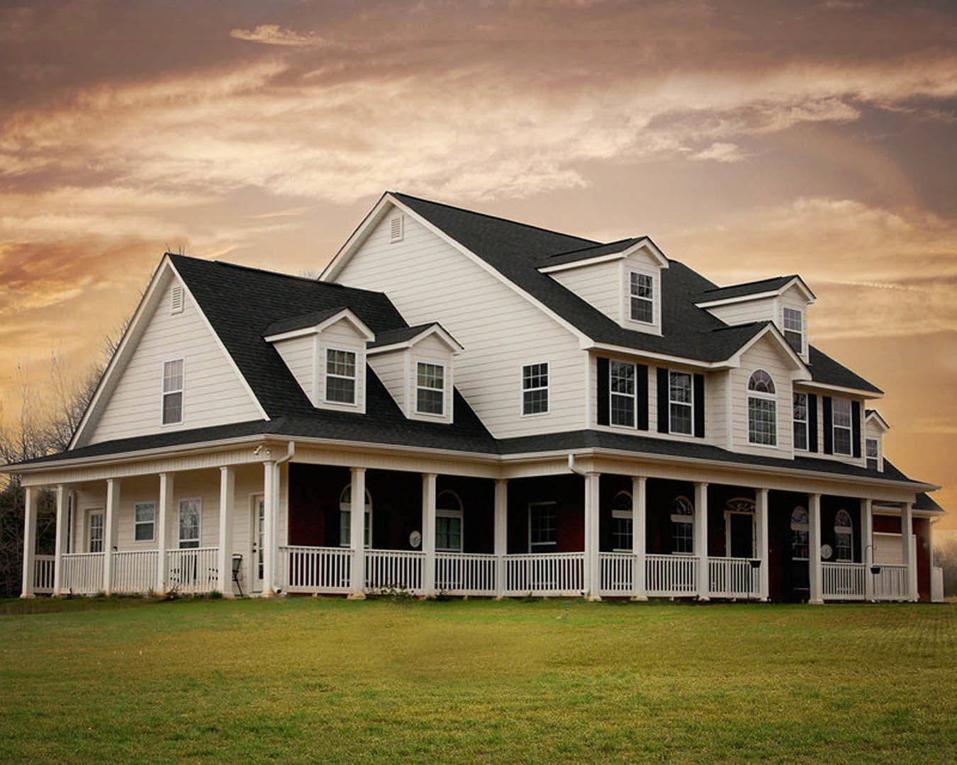 White two-story home with wide front porch, multi-pane windows, and black-striped white fence, set in grassy yard under cloudy sky.