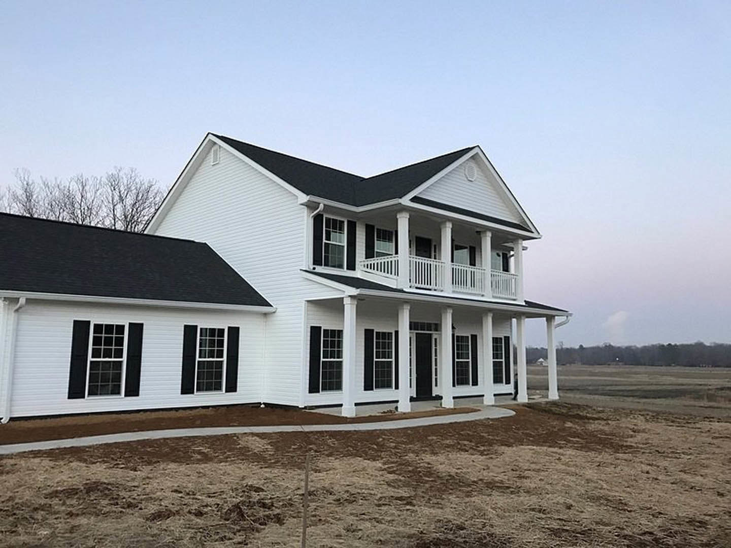 White siding house with black roof and black shutters, white framed windows, covered porch, dirt patch in front yard, blue sky overhead