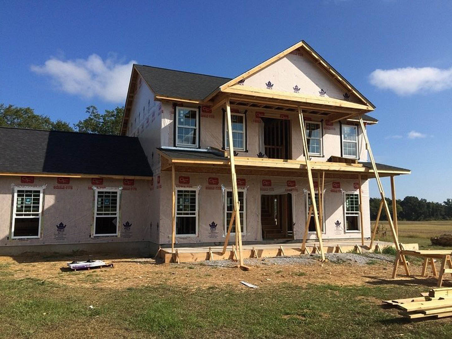 Wood-framed house under construction with scaffolding, partially installed windows and doors, Grouseland historic mansion visible in the background
