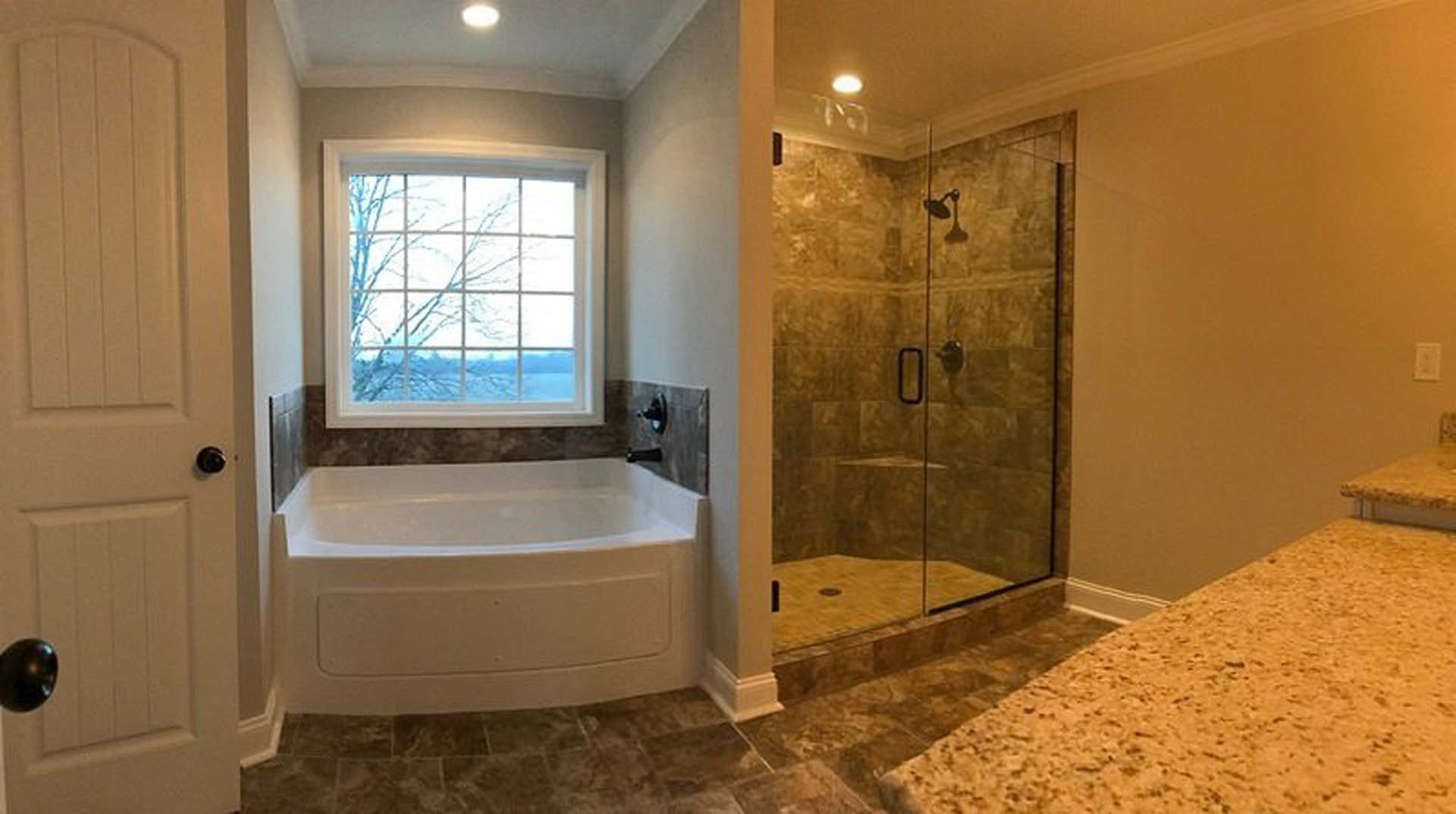 Bathroom featuring a frameless glass shower, freestanding white tub with brown stone surround, black faucet fixtures, white countertop with circular sink, large window overlooking