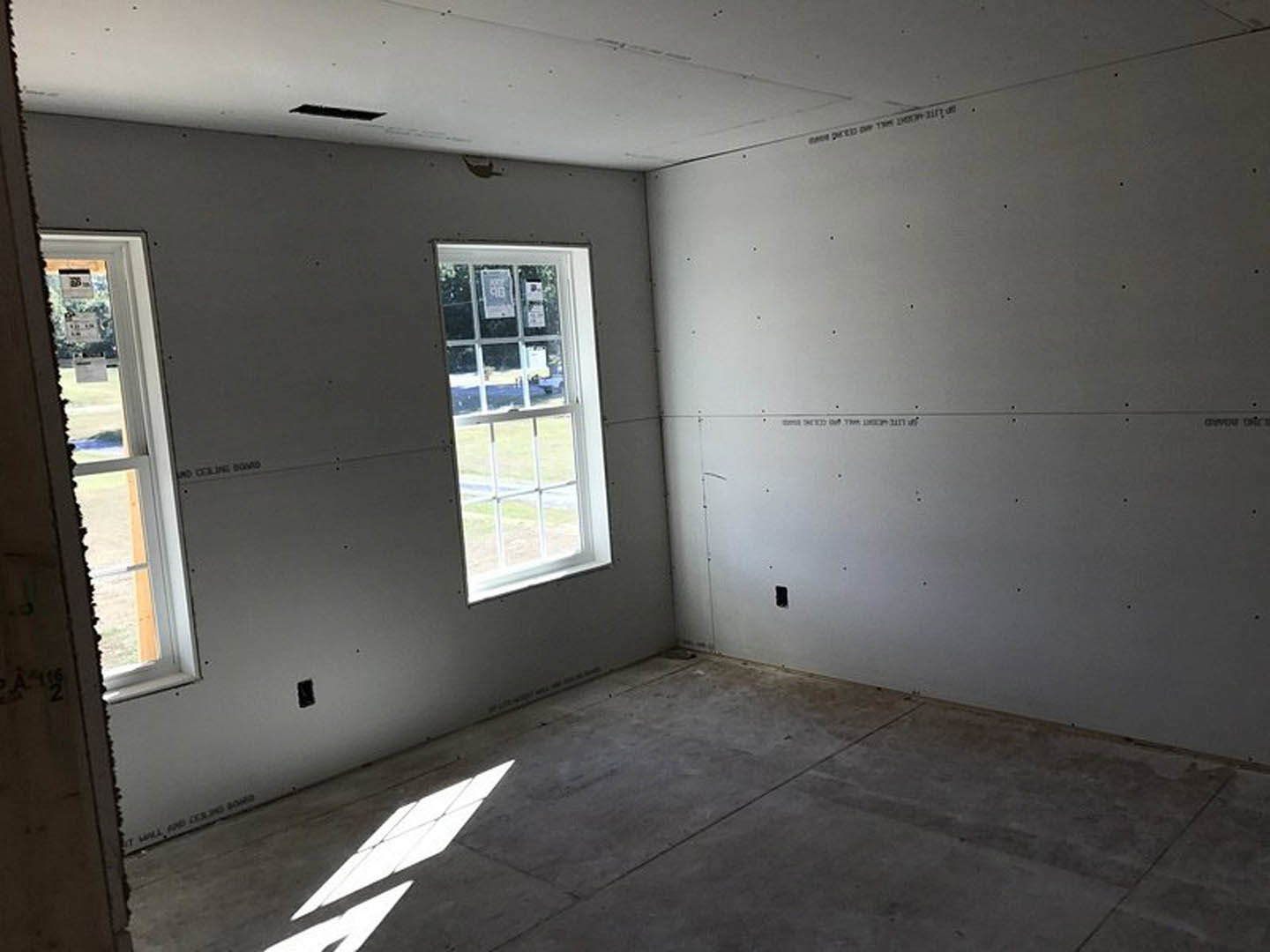 Spacious room with large windows, white plaster walls, and smooth concrete flooring, sunlight streaming through glass panes