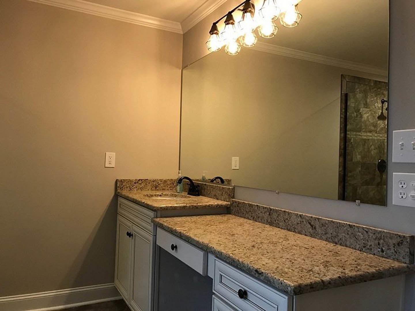 Bathroom with marble countertop, rectangular mirror above sink, white cabinetry, chrome faucet, tiled wall, and cluster of exposed light bulbs