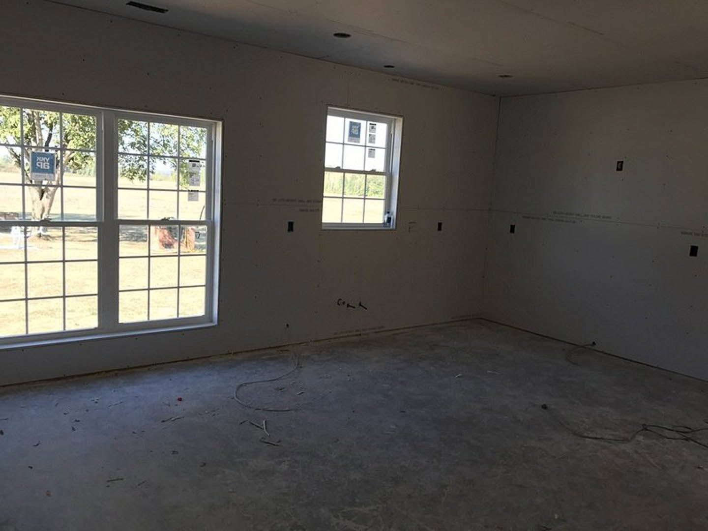 Spacious room featuring large windows, concrete floor, white plaster walls, and ceiling; daylight streams in, highlighting minimalist finishes and a view of a tree outside.
