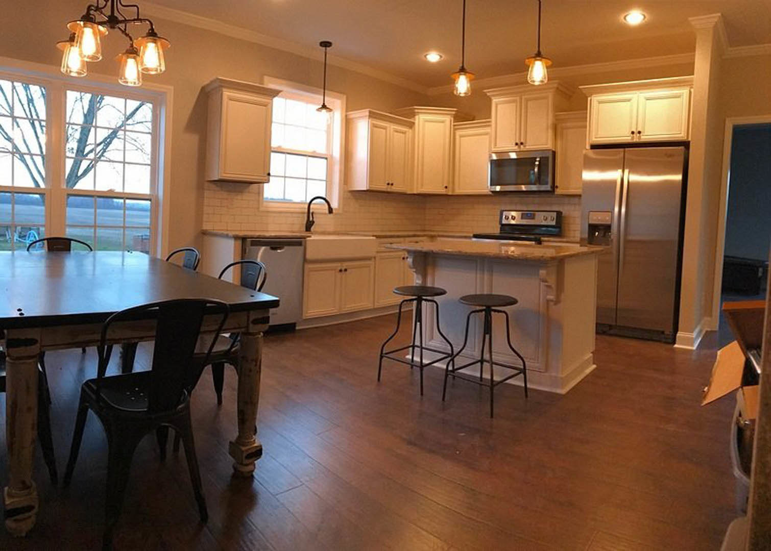 Modern kitchen featuring wood cabinetry, stainless steel refrigerator, dining table with chairs, light fixture overhead, and neutral walls with tile flooring