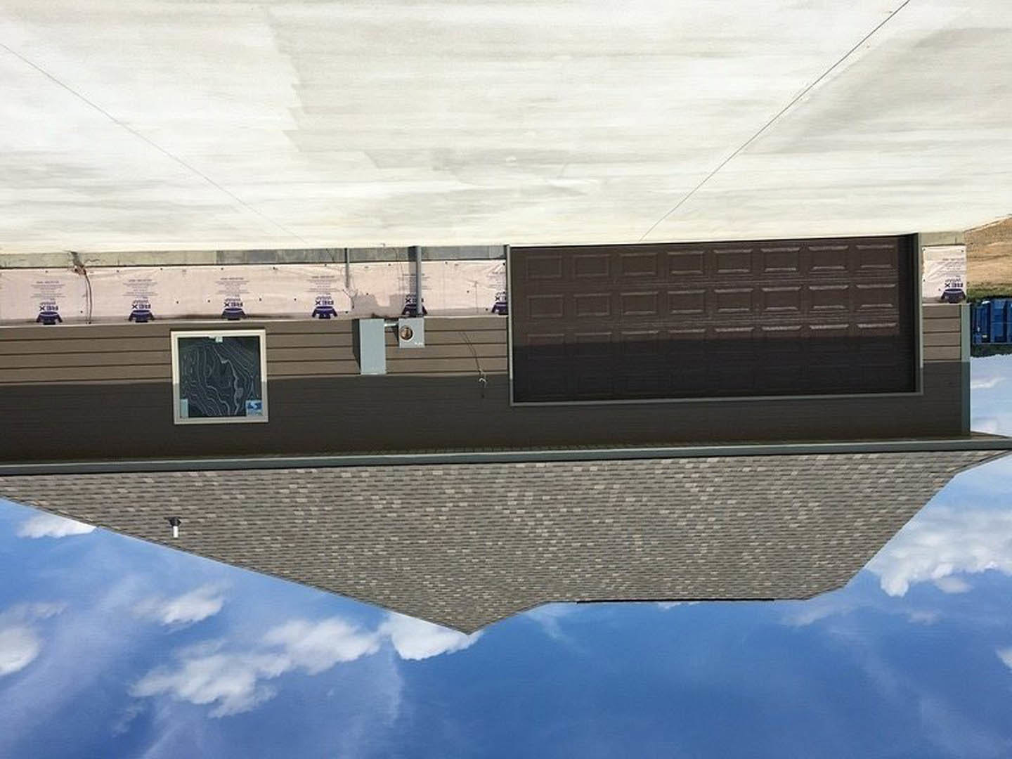 Gray stucco exterior with a white-framed window and dark wood front door beneath a sloped roof, set against a cloudy sky