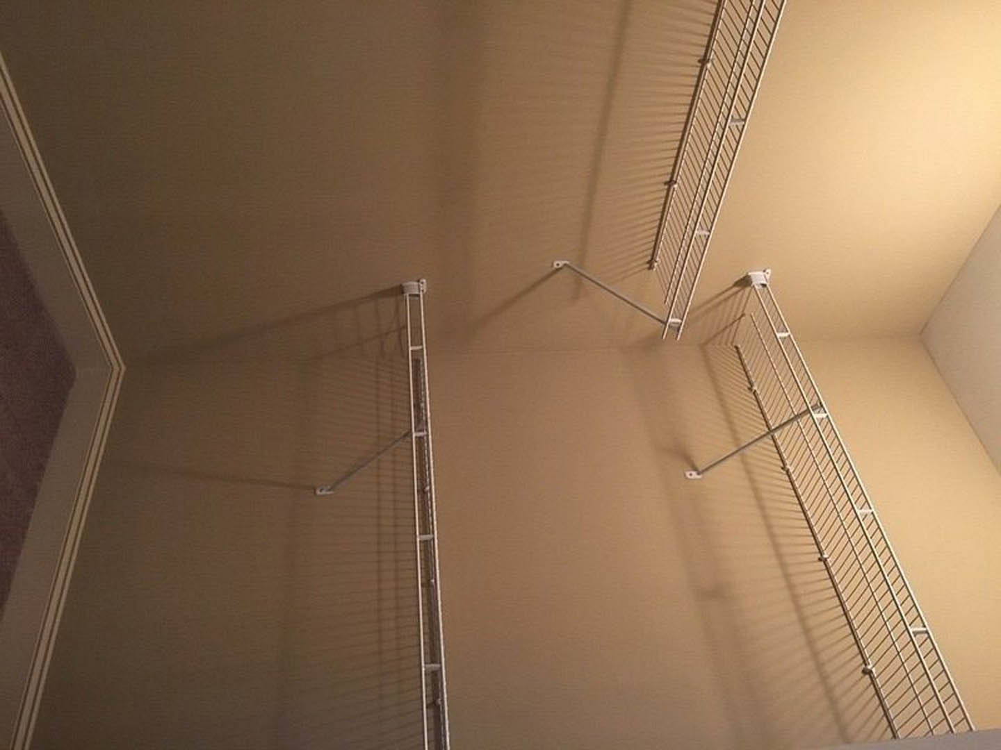 White metal ladder mounted vertically on a plaster wall beneath recessed ceiling lighting in a modern interior space.