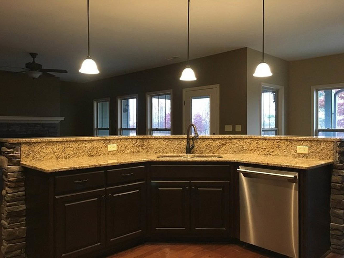 Granite countertops with tile backsplash, stainless steel sink, wood cabinetry, and stone pillar in custom kitchen