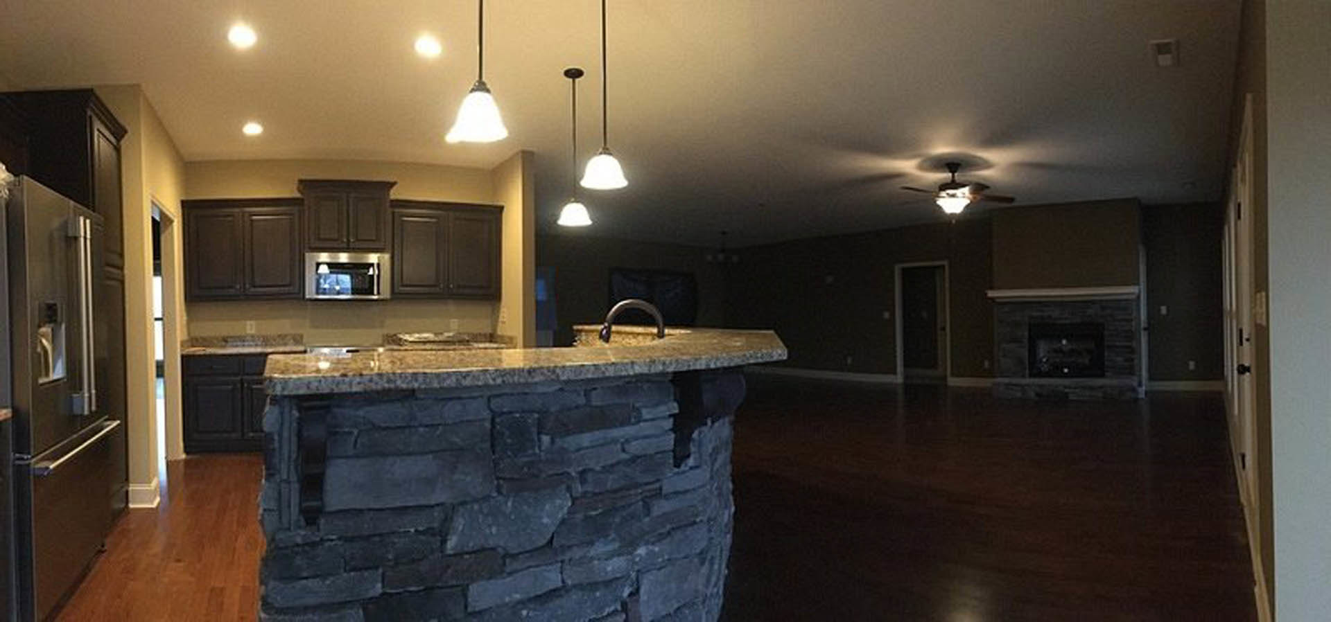 Kitchen with stone accent wall, ceiling fan, light fixture, cabinetry, countertop, stainless steel refrigerator, and window.