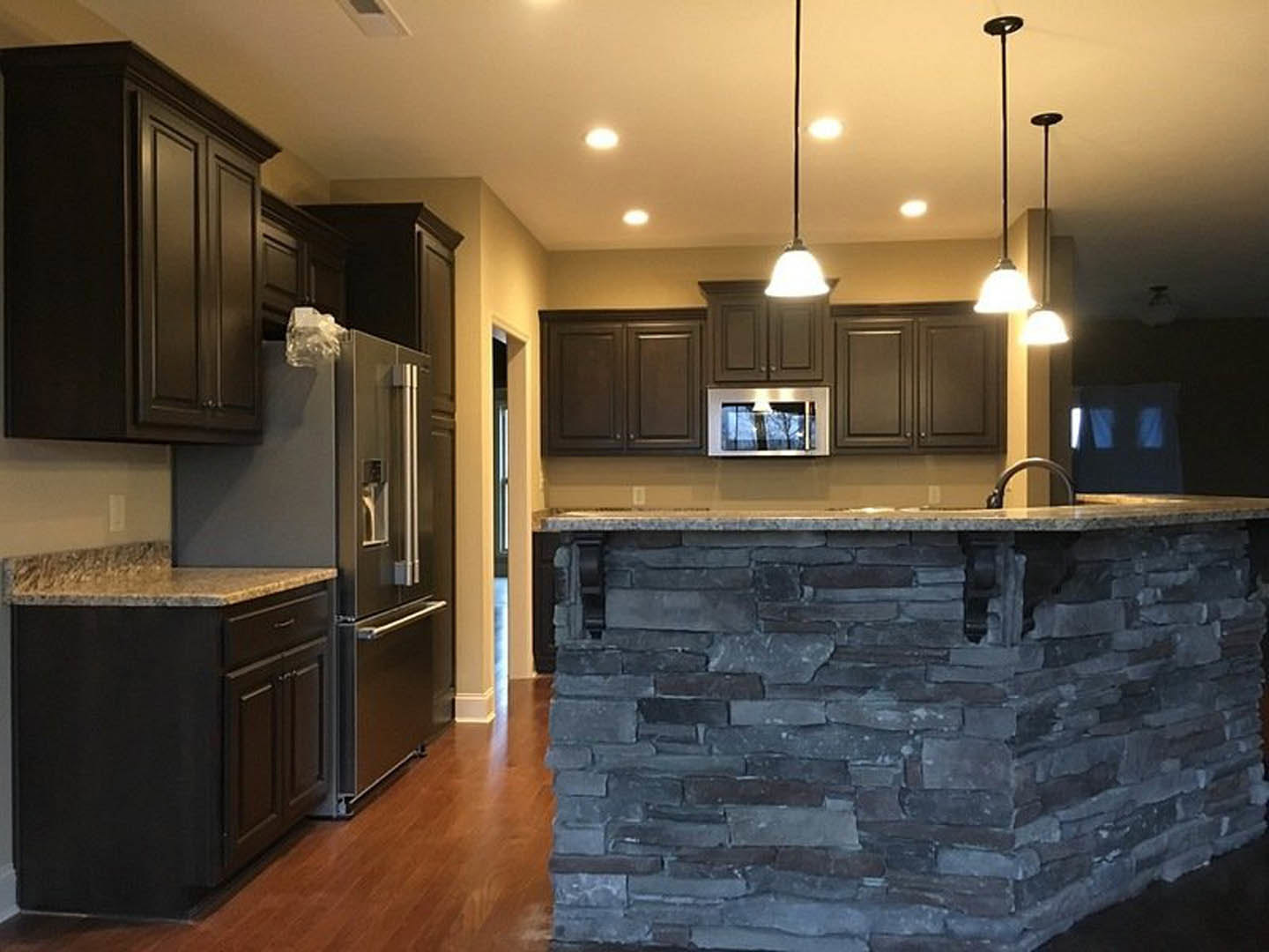 Kitchen with stone island, stainless refrigerator, granite countertops, wood cabinetry, and light fixtures on ceiling