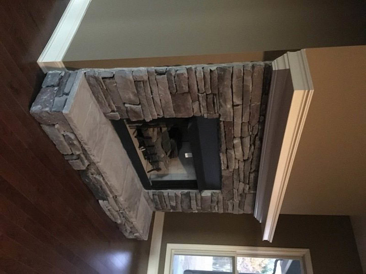 Stone fireplace with white mantel, hardwood floors, white-framed window with sheer curtains, cat resting on hearth, plaster walls with crown molding